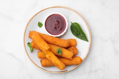 Photo of Tasty fried mozzarella sticks served with tomato sauce and basil on white marble table, top view