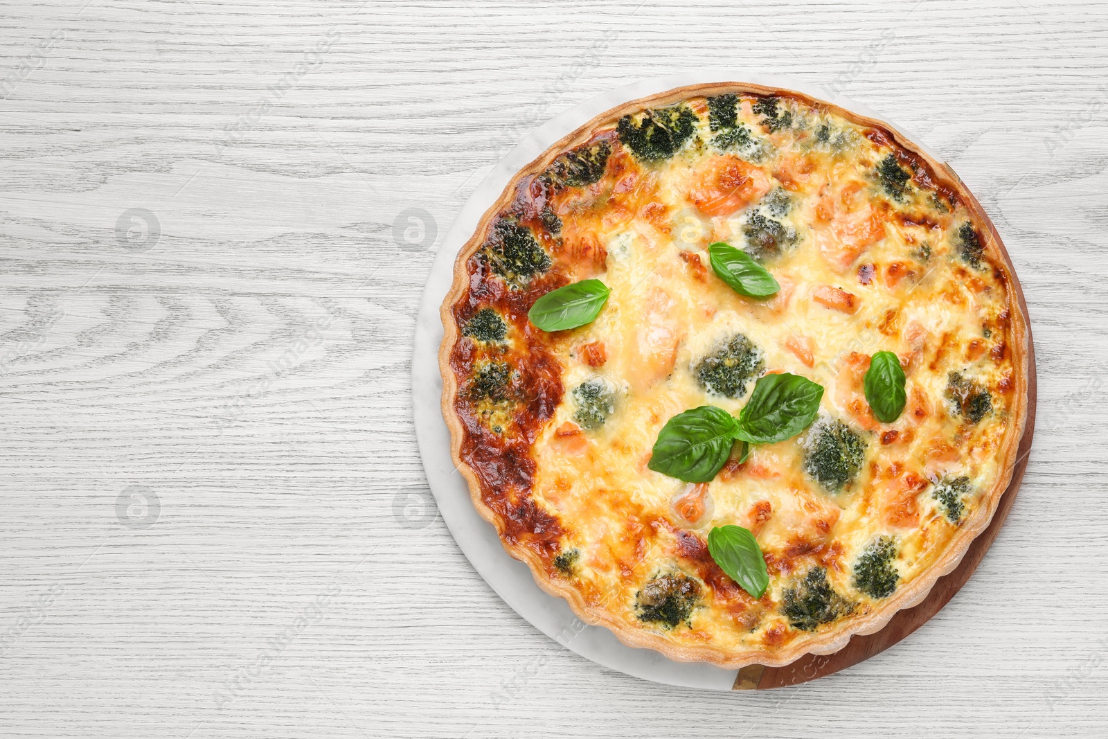 Photo of Delicious homemade quiche with salmon, broccoli and basil leaves on wooden table, top view. Space for text