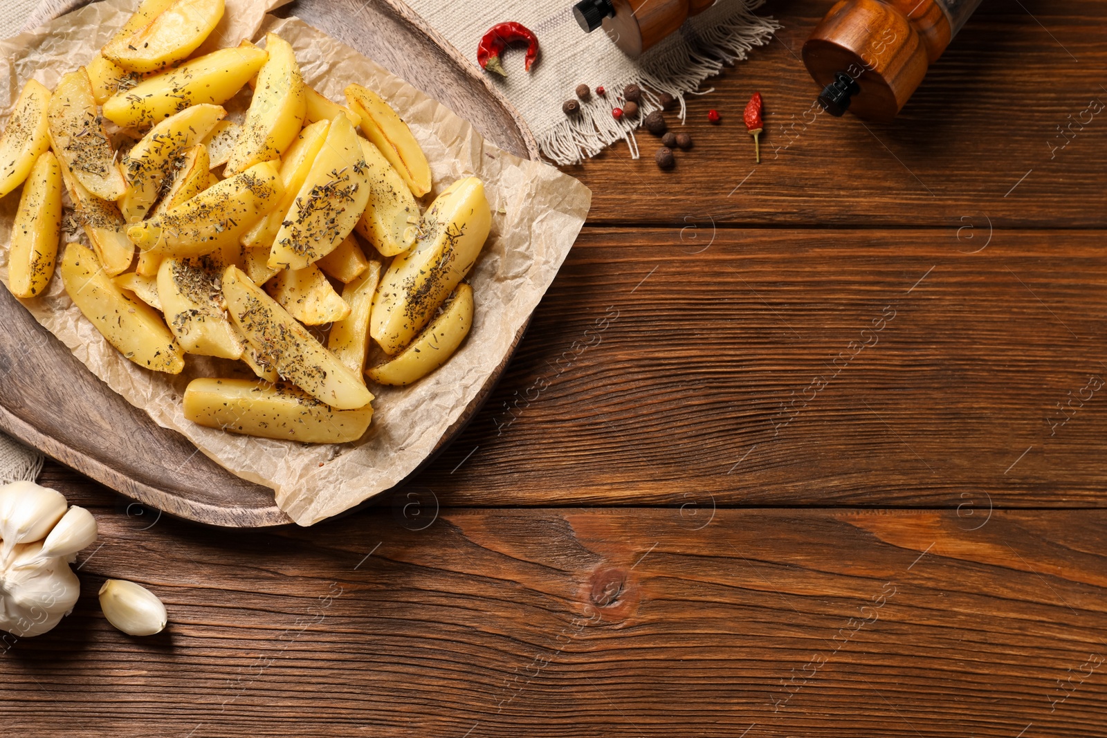 Photo of Board with tasty baked potato wedges and spices on wooden table, flat lay. Space for text