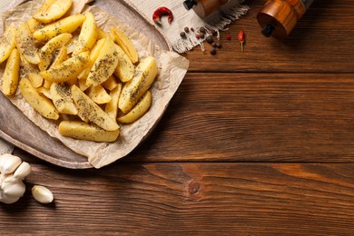 Photo of Board with tasty baked potato wedges and spices on wooden table, flat lay. Space for text