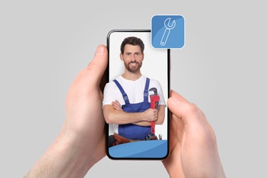 Image of Find plumber. Man using mobile phone on light grey background, closeup. Specialist looking out of gadget