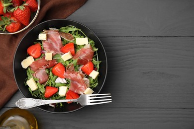 Photo of Tasty salad with brie cheese, prosciutto and strawberries served on grey wooden table, flat lay. Space for text