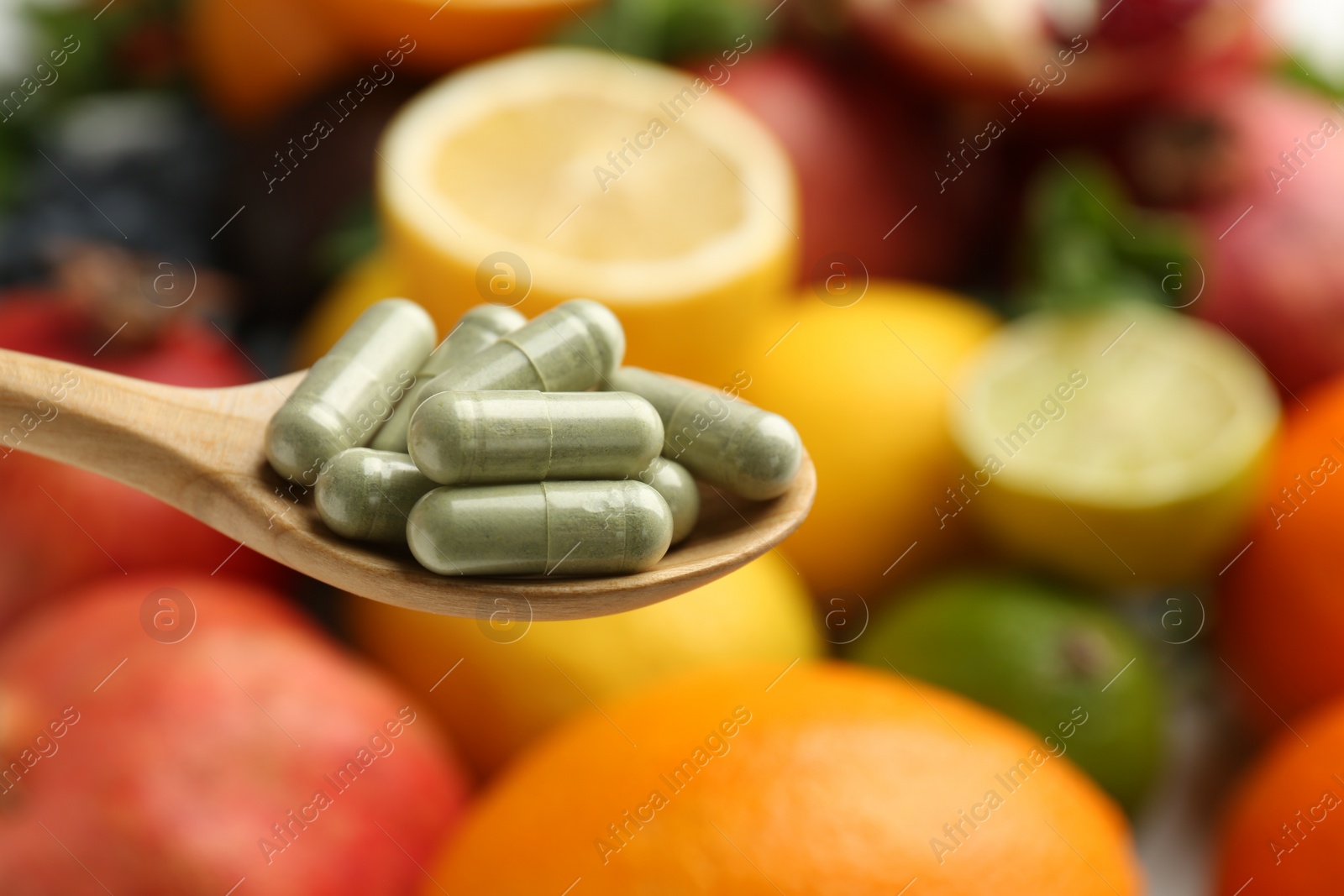 Photo of Vitamin pills in spoon against fresh fruits, closeup. Space for text