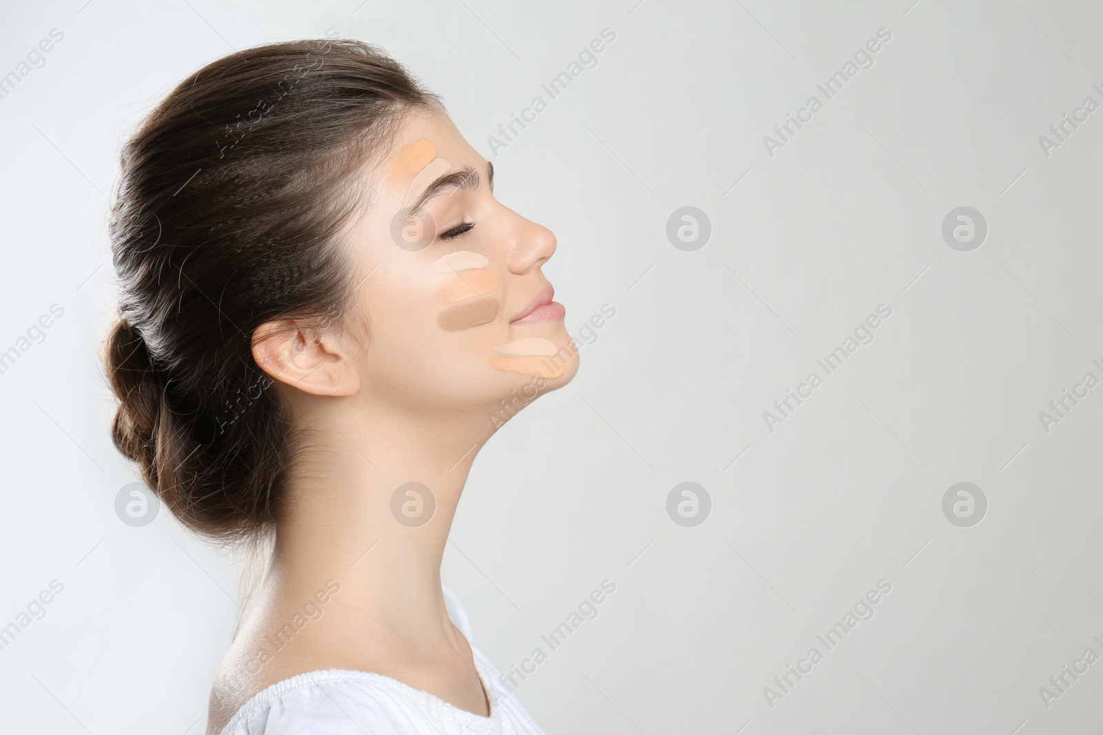 Photo of Beautiful girl on light grey background. Using concealers and foundation for face contouring