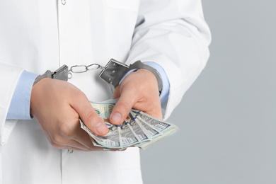 Doctor in handcuffs with bribe on grey background, closeup. Corrupted medicine