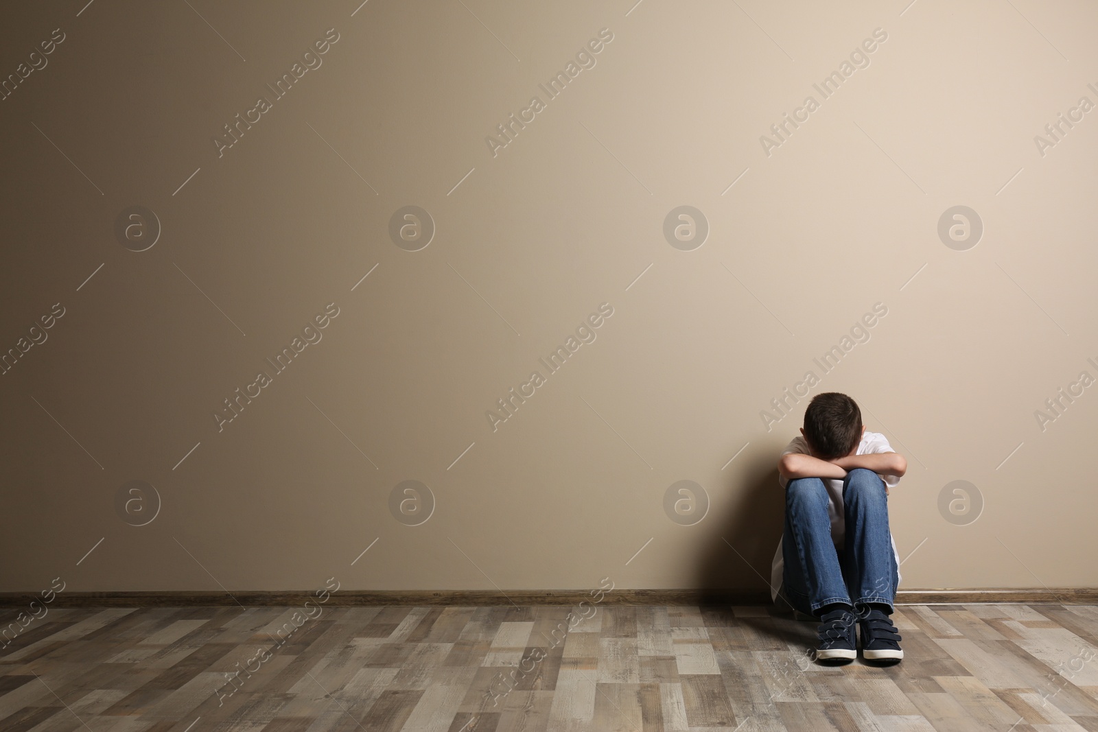 Photo of Upset boy sitting on floor at color wall. Space for text