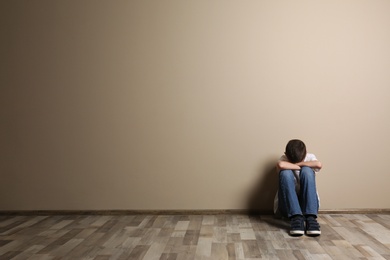 Photo of Upset boy sitting on floor at color wall. Space for text