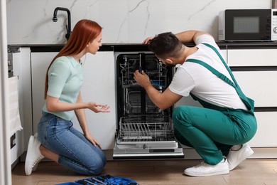 Photo of Woman looking how serviceman repairing her dishwasher in kitchen