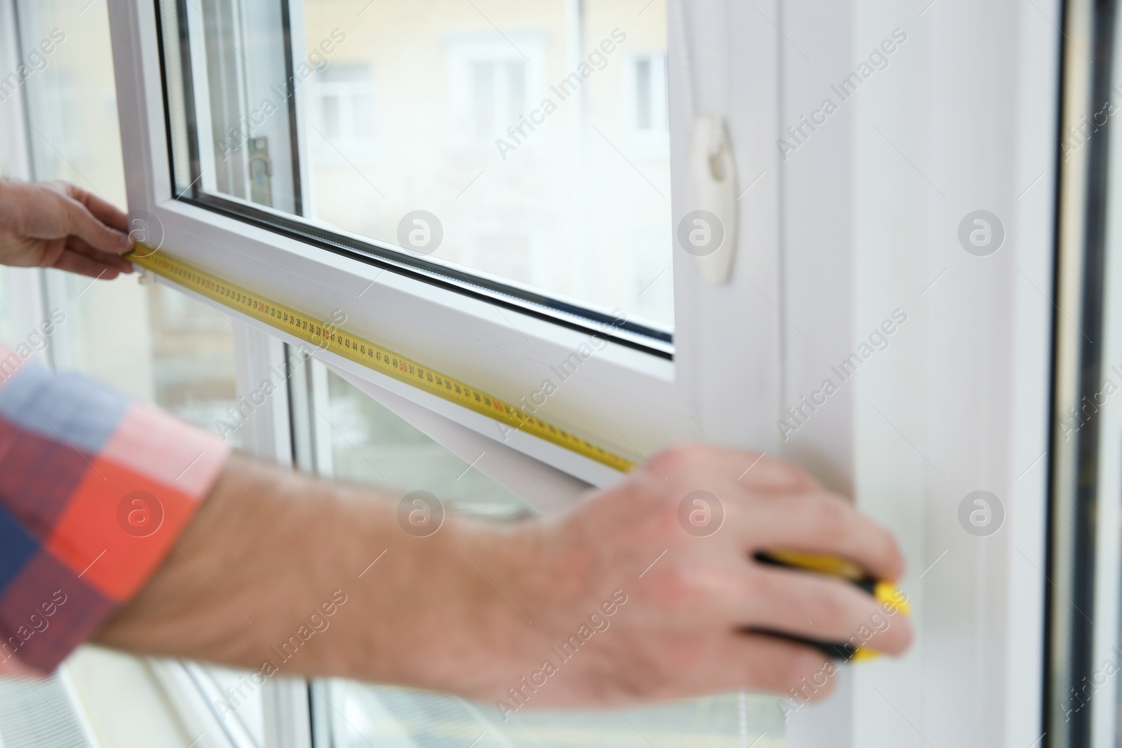 Photo of Construction worker measuring plastic window indoors, closeup. Professional installation