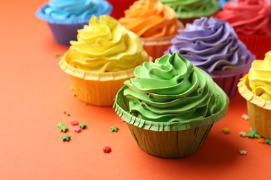 Photo of Delicious bright cupcakes and sprinkles on coral background, closeup