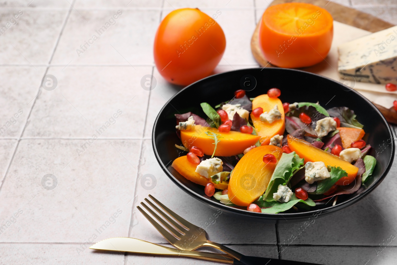 Photo of Delicious persimmon salad, knife and fork on tiled surface, space for text