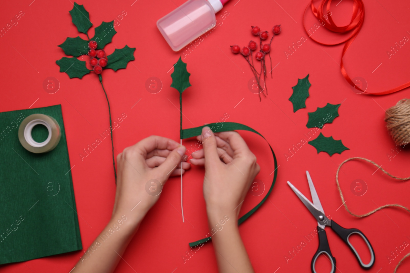 Photo of Woman making mistletoe branch on red background, top view