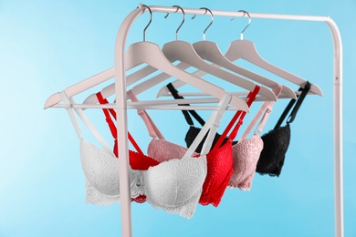 Photo of Hangers with beautiful lace bras on rack against blue background. Stylish underwear