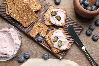 Photo of Tasty sandwiches with cream cheese and blueberries on wooden table, flat lay