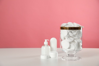 Jar with cotton pads on white table against pink background. Space for text