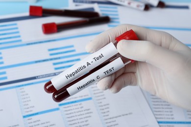 Scientist holding tubes with blood samples for hepatitis virus test near laboratory form, closeup