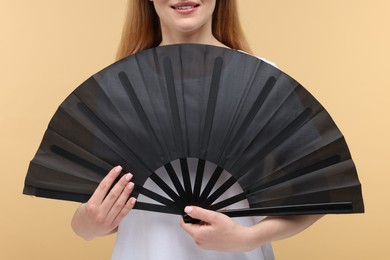 Woman with black hand fan on beige background, closeup