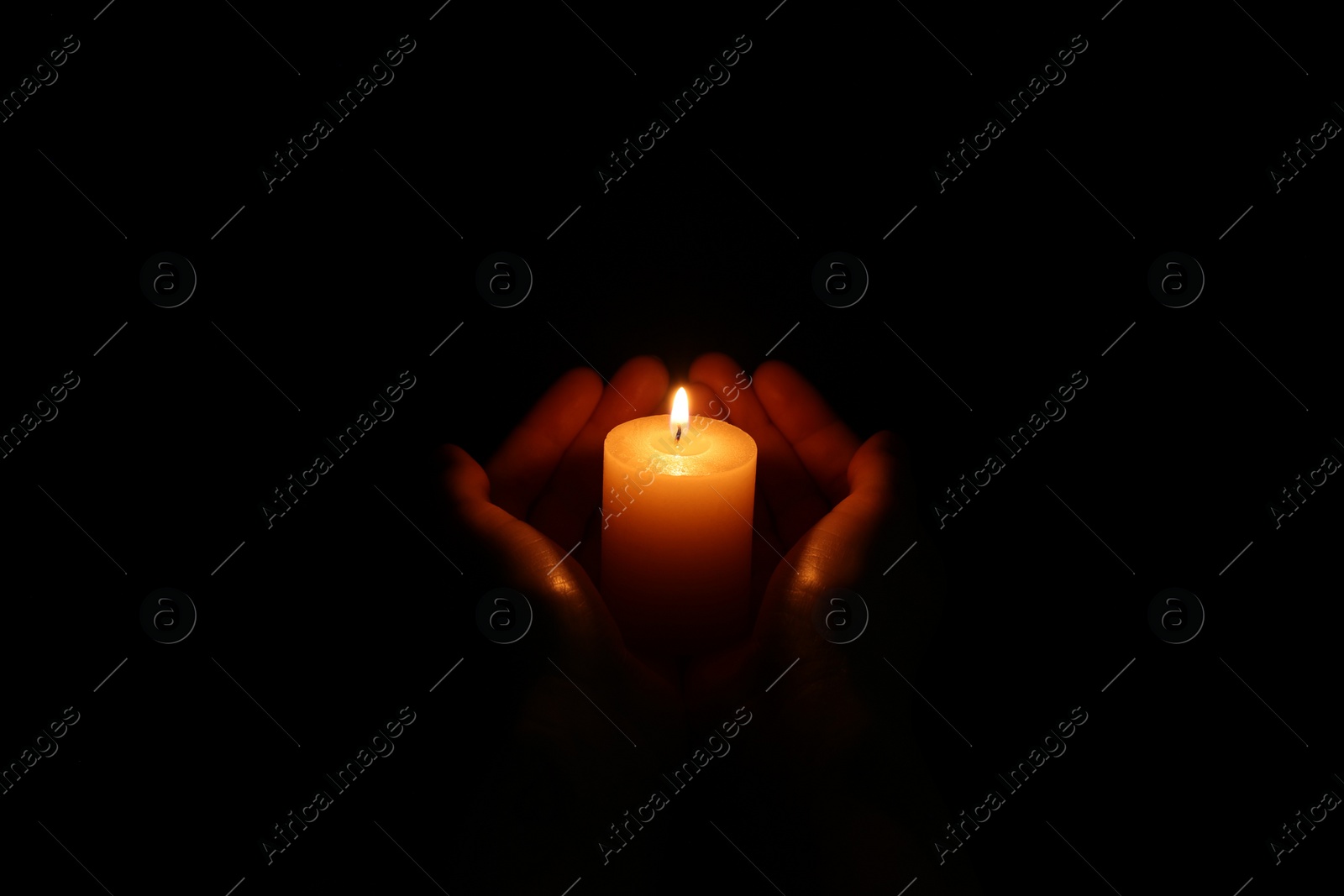 Photo of Woman holding burning candle in hands on black background, closeup