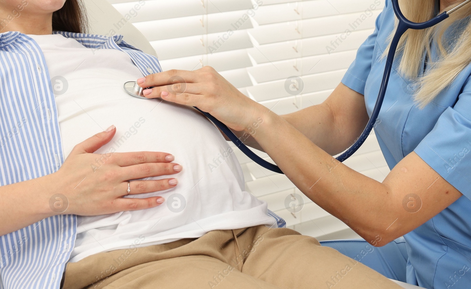 Photo of Pregnancy checkup. Doctor with stethoscope listening baby's heartbeat in patient's tummy in clinic, closeup