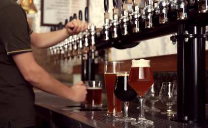 Bartender pouring fresh beer into glass in pub, closeup