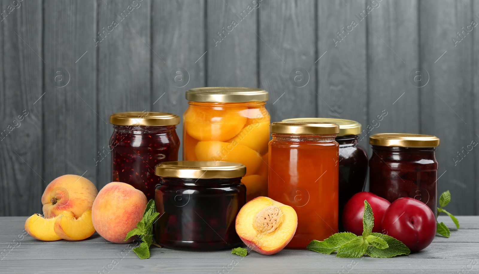 Photo of Glass jars with different pickled fruits and jams on grey wooden background