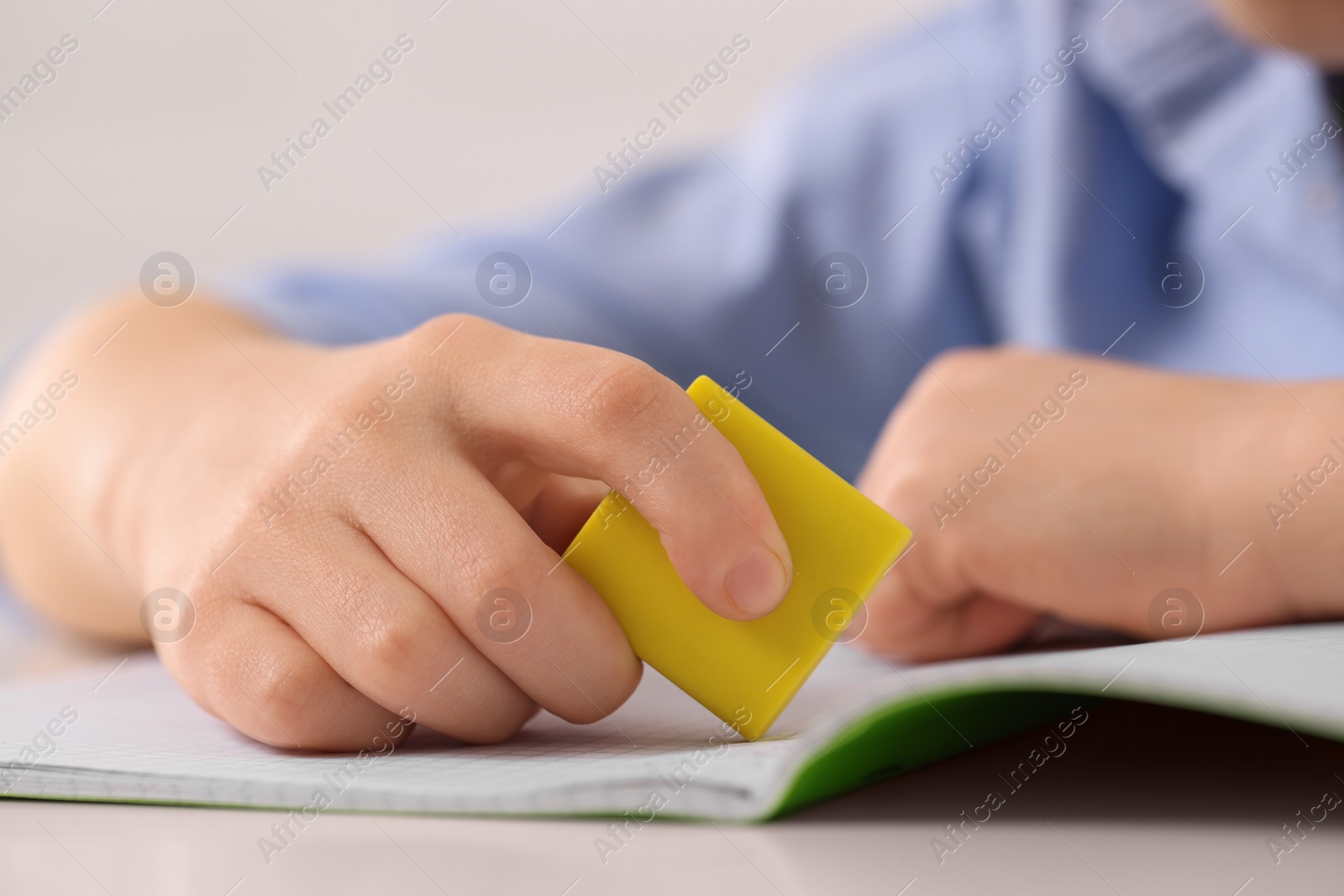 Photo of Boy erasing mistake in his notebook at white desk, closeup