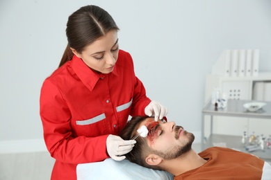 Photo of Nurse cleaning young man's head injury in clinic. First aid