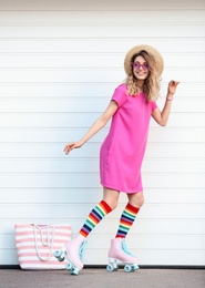 Happy young woman with retro roller skates near white garage door