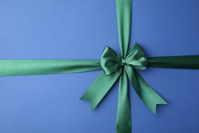 Green satin ribbon with bow on blue background, top view