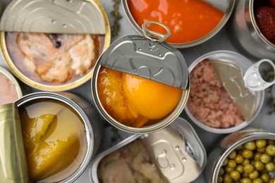 Open tin cans with different preserved products on grey table, flat lay