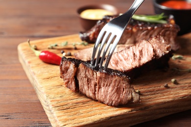 Photo of Fork with delicious barbecued steak on wooden table