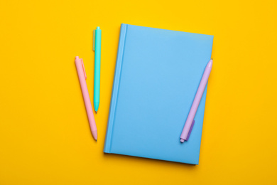 Photo of Light blue notebook and pens on yellow background, flat lay