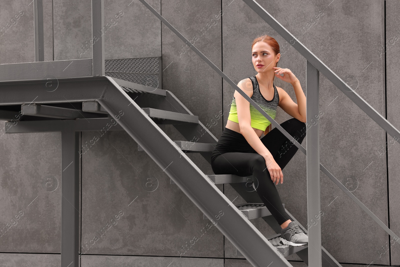 Photo of Beautiful woman in stylish gym clothes sitting on stairs on street