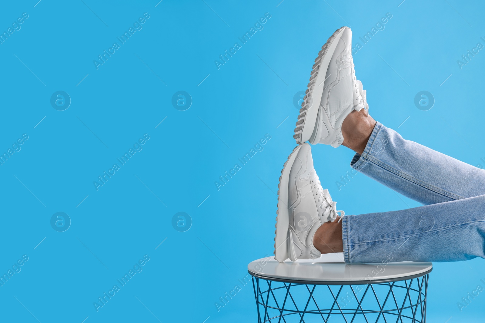 Photo of Man wearing stylish sneakers on white table against light blue background, closeup. Space for text