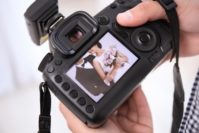 Professional photographer holding camera with lovely wedding couple on display, closeup