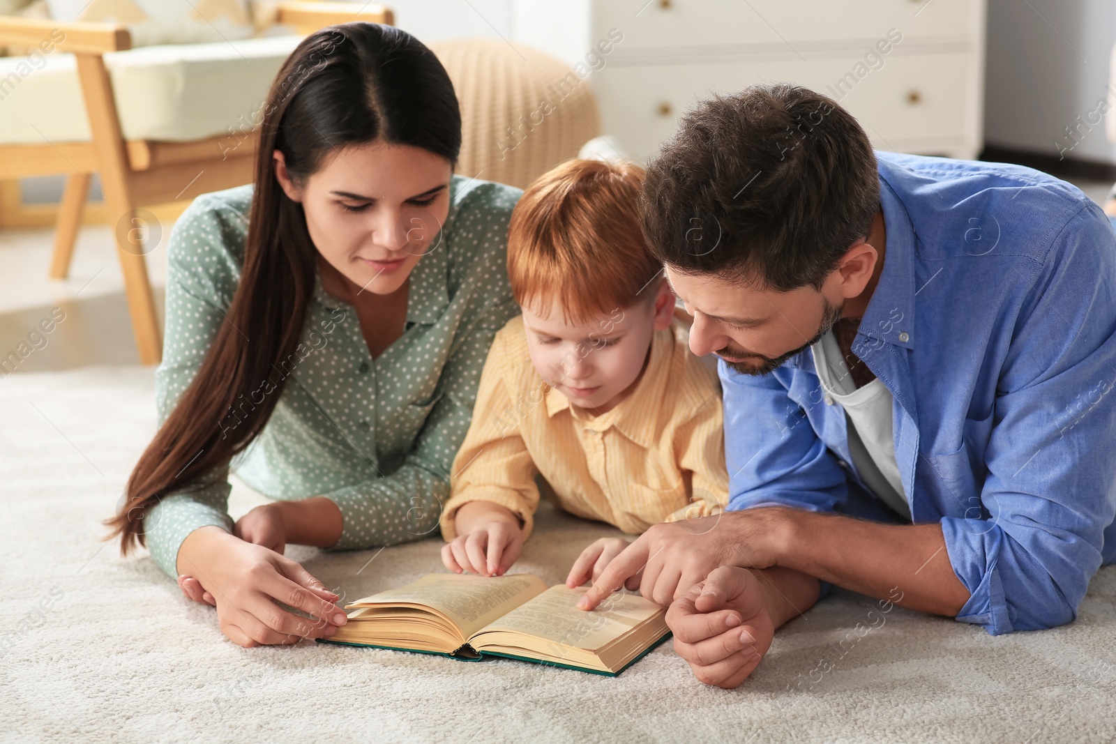 Photo of Happy family reading book together on floor in living room at home