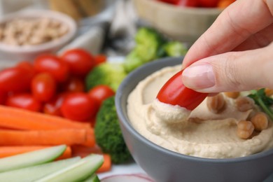 Photo of Woman dipping tomato into hummus at table, closeup