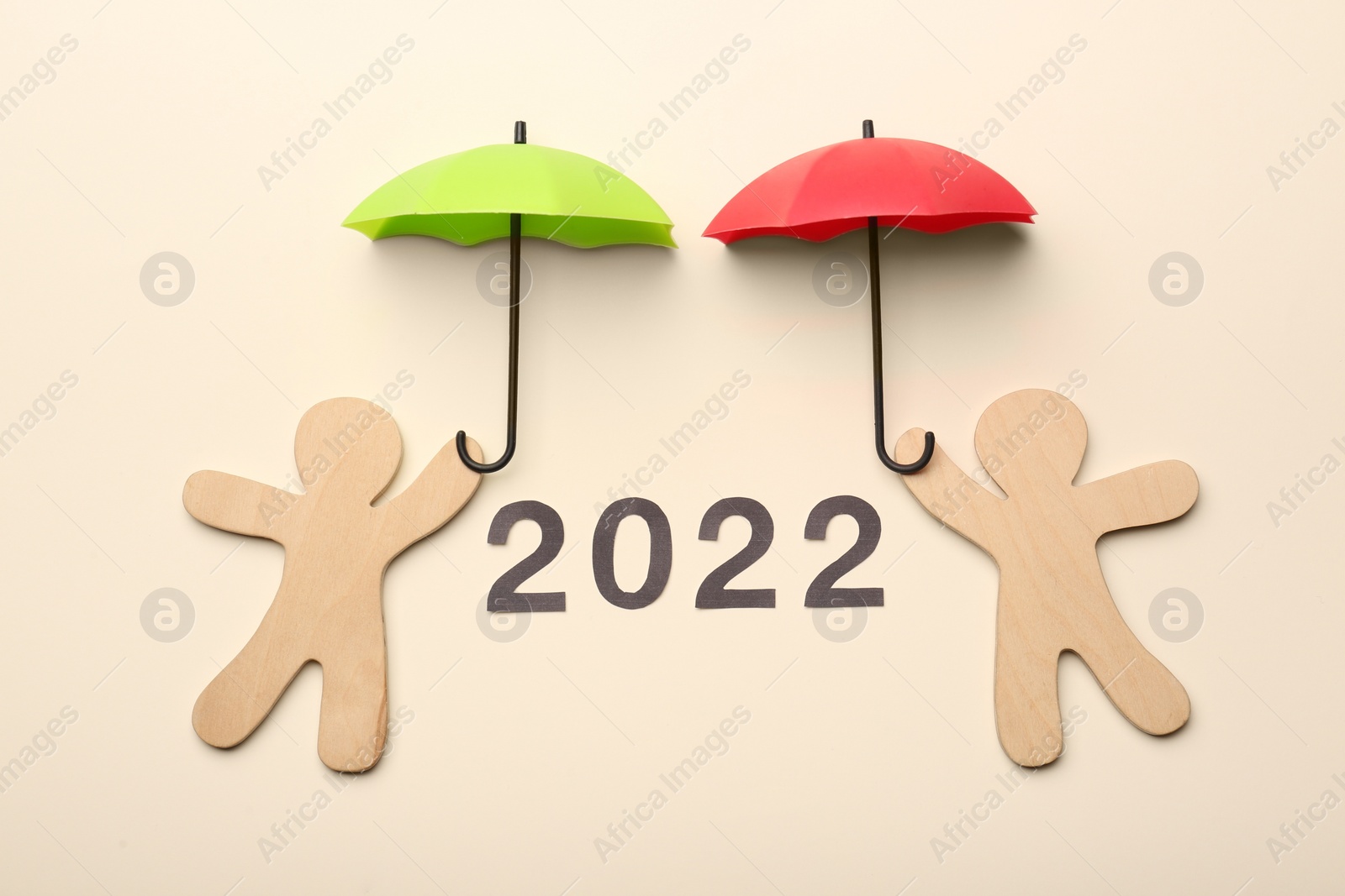 Photo of Mini umbrellas, figures of people and number 2022 on beige background, flat lay