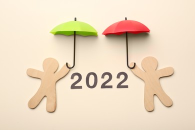 Photo of Mini umbrellas, figures of people and number 2022 on beige background, flat lay