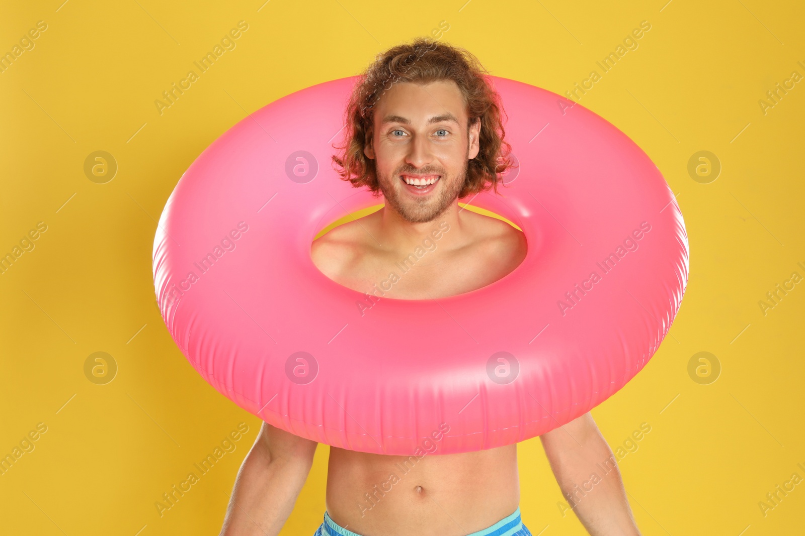 Photo of Attractive young man in swimwear with pink inflatable ring on yellow background
