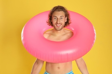 Photo of Attractive young man in swimwear with pink inflatable ring on yellow background