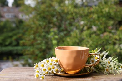 Cup of delicious chamomile tea and fresh flowers outdoors on sunny day, space for text