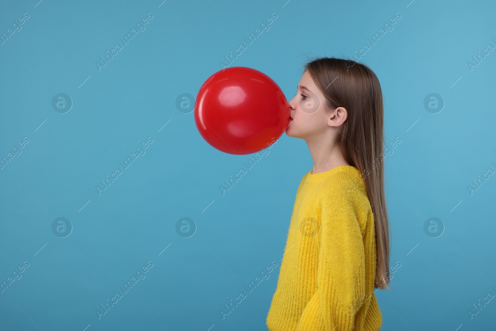 Photo of Cute girl inflating red balloon on light blue background, space for text