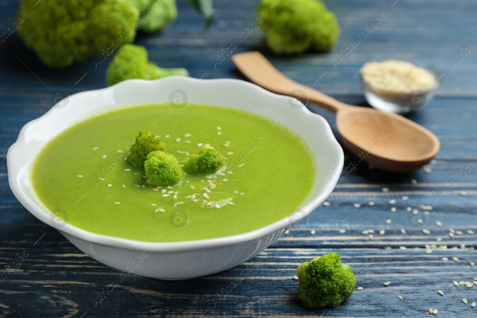 Photo of Bowl of broccoli cream soup with sesame seeds served on blue wooden table