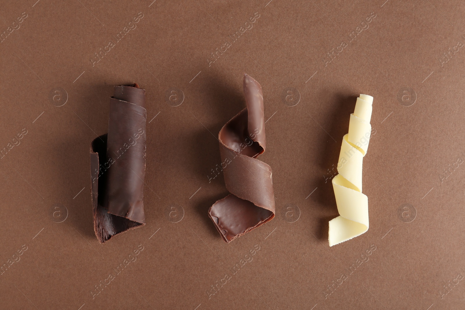 Photo of Different chocolate curls on color background, top view