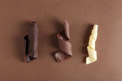 Different chocolate curls on color background, top view