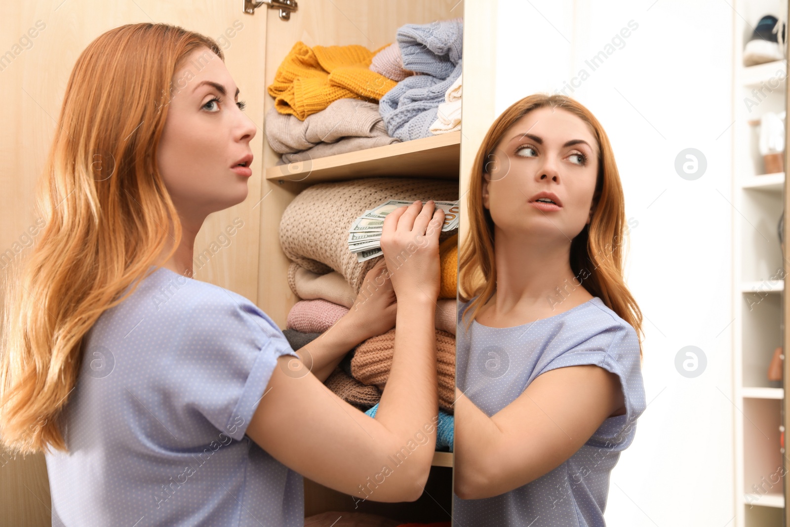 Photo of Worried woman hiding money between clothes in wardrobe indoors. Financial savings