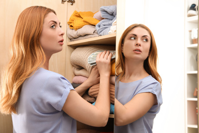 Worried woman hiding money between clothes in wardrobe indoors. Financial savings