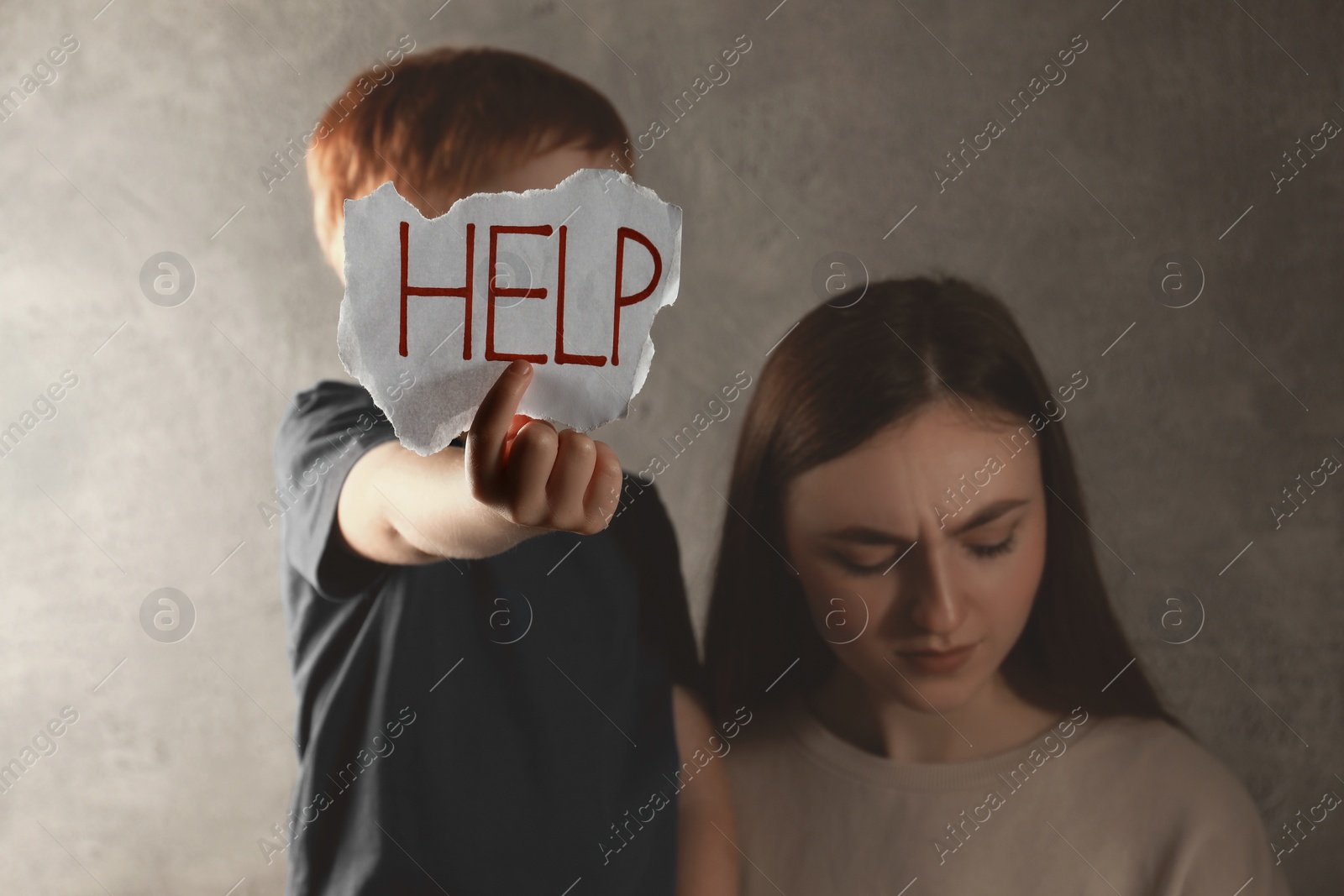 Photo of Scared mother and little boy holding piece of paper with word Help against light grey background. Domestic violence concept