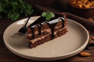 Photo of Piece of tasty homemade chocolate cake with mint on wooden table, closeup